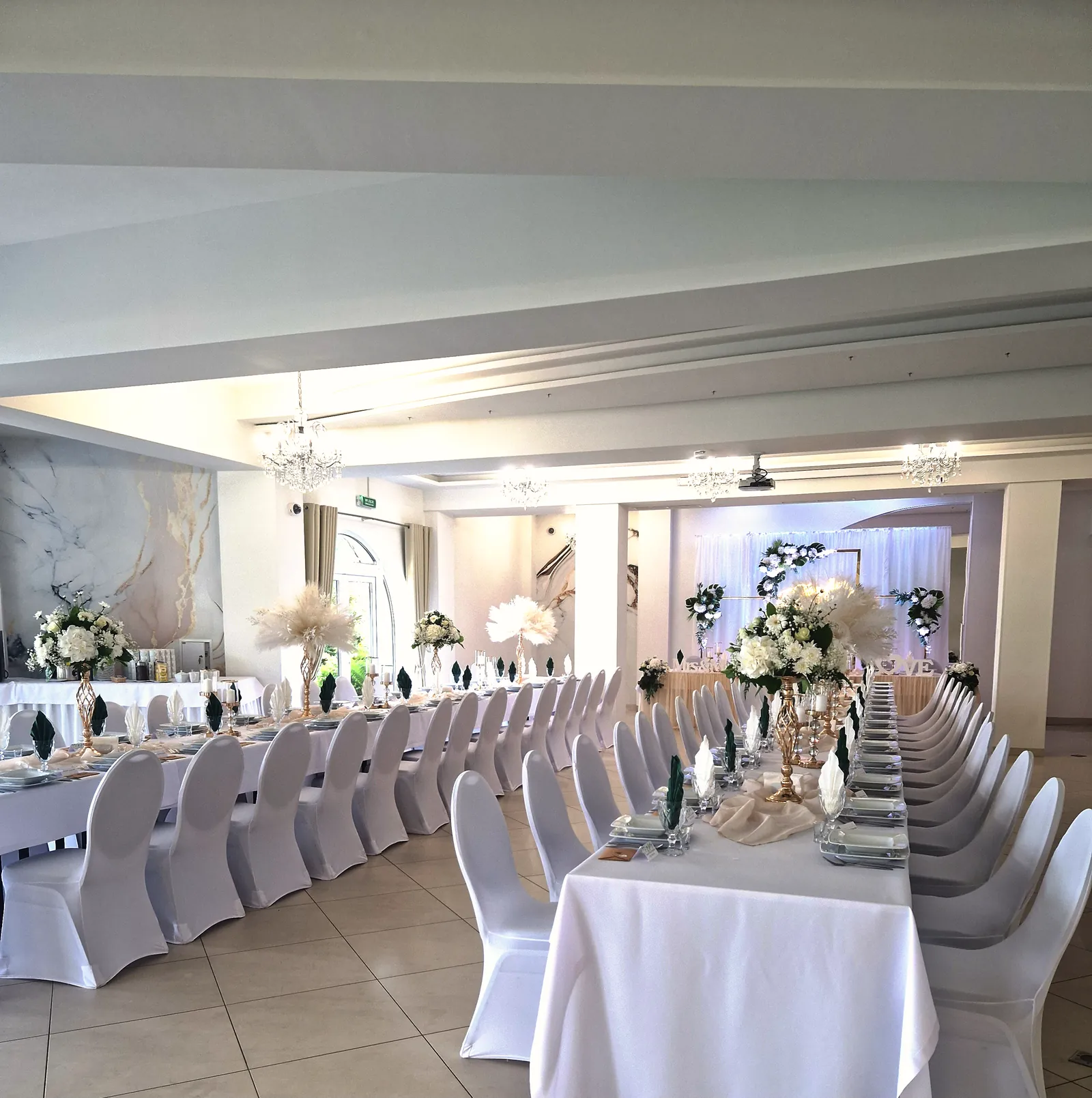 Sala Diamentowa nakryta do wesela — długie stoły z białymi pokrowcami na krzesłach, złote świeczniki z białymi kompozycjami kwiatowymi, kryształowe żyrandole