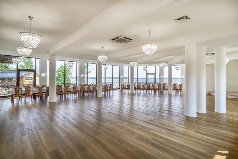 Sala Złota — drewniany parkiet, białe słupy, kryształowe żyrandole i panoramiczne okna z widokiem na jezioro
