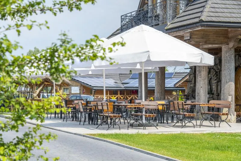 Taras restauracji z białymi parasolami i stolikami, otoczony zielenią
